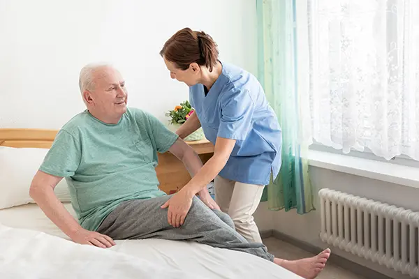 Nursing home – home caregiver helping an elderly man out of bed