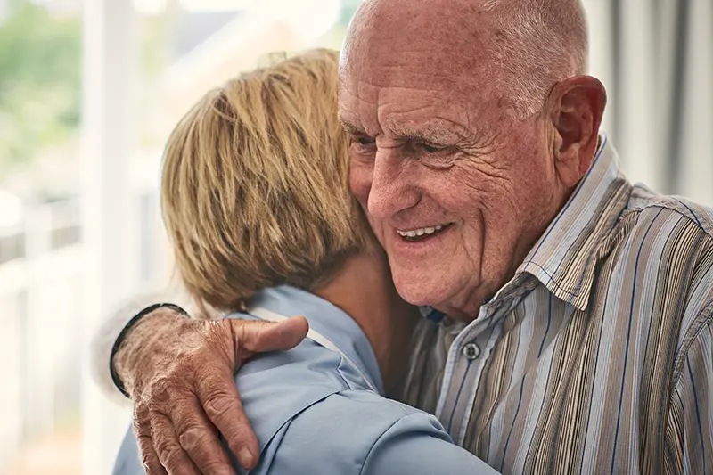 Female home carer hugging senior male patient at care home
